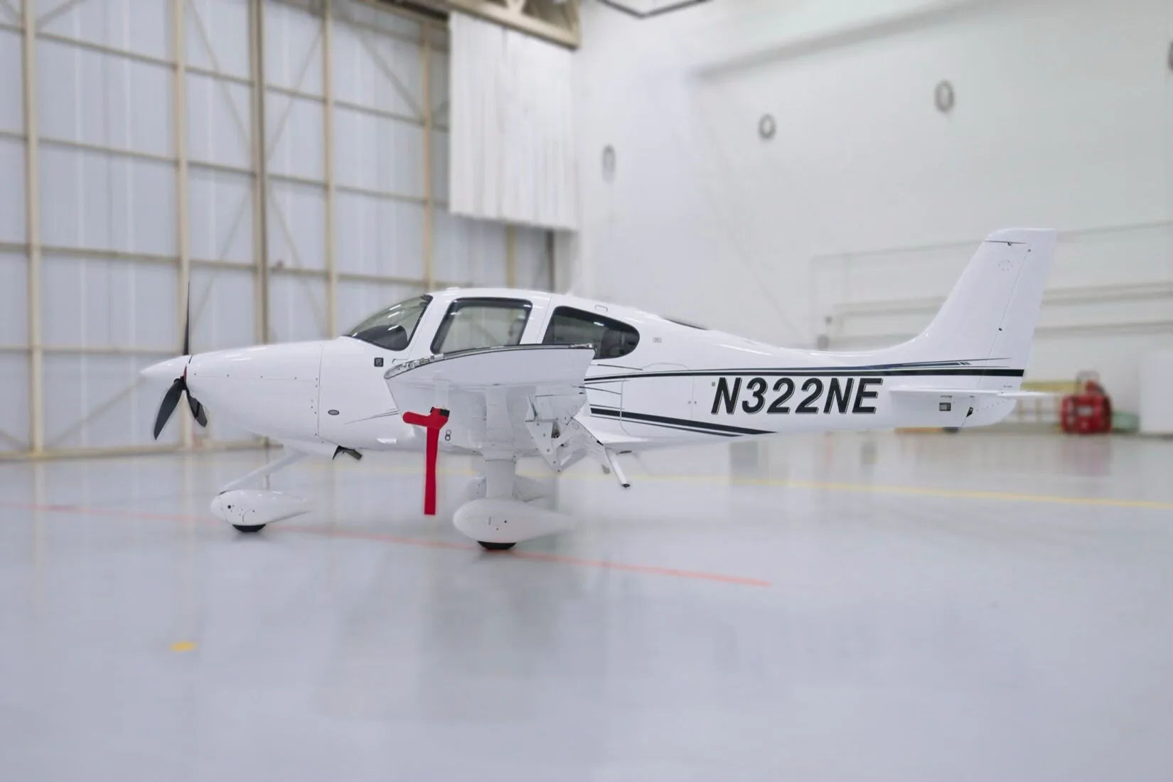 A white Cirrus SR22 aircraft with black and blue stripes, registration N322NE, parked in a hangar.