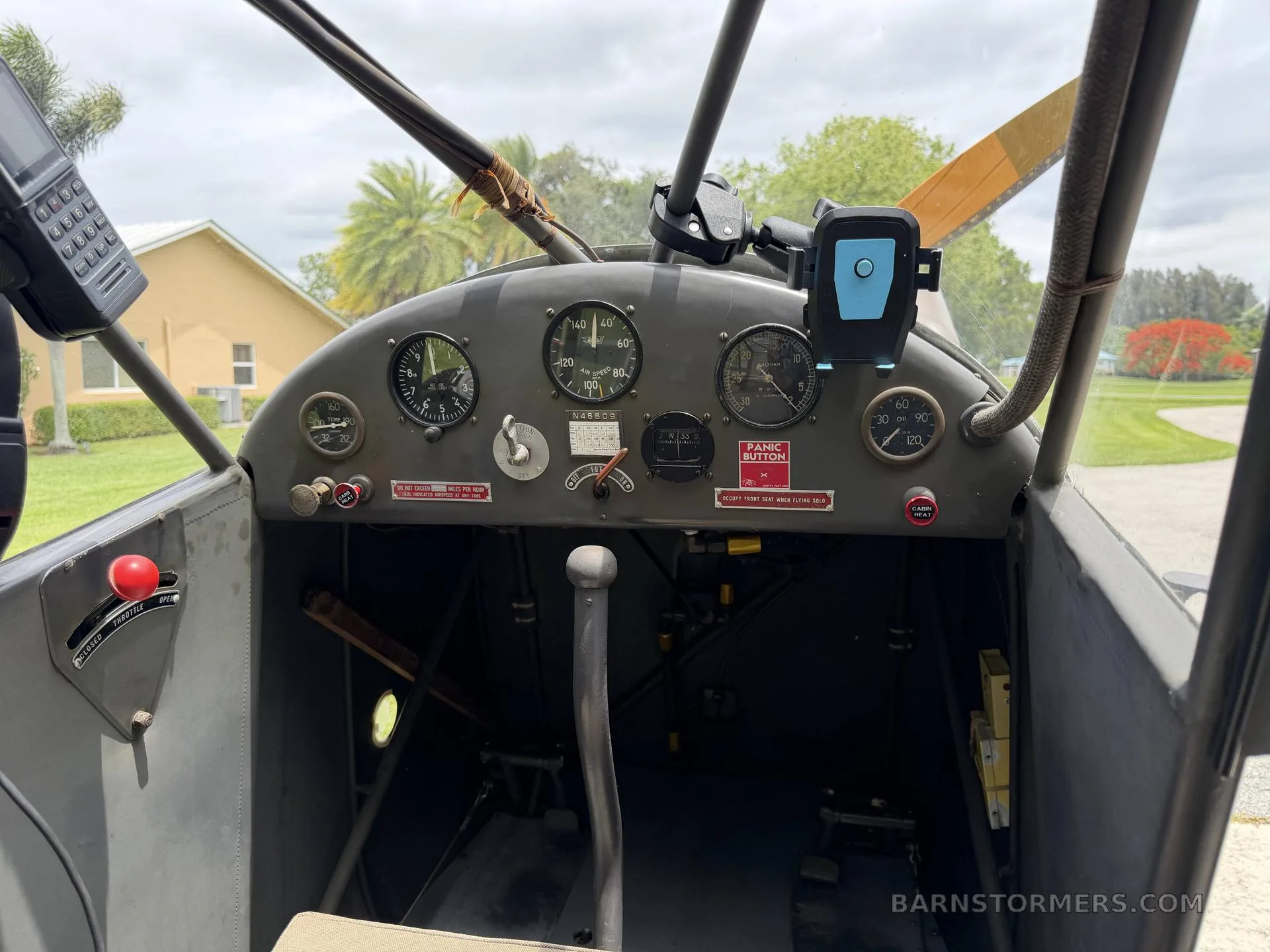 The simple instrument panel and controls of a vintage aircraft cockpit, with a view of the propeller and outside.