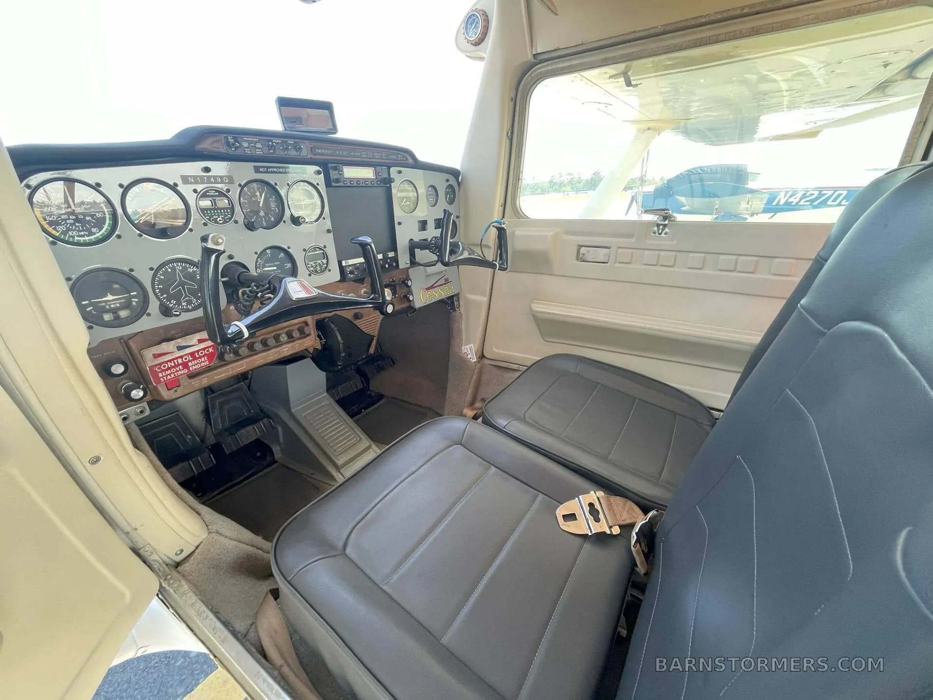 The cockpit of a Cessna 172 shows the instrument panel, control yoke, and two dark gray seats.