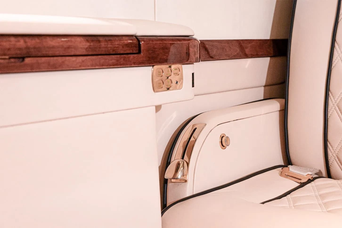 A close-up of a cream leather seat with gold accents and a control panel on the side wall of the private jet cabin.
