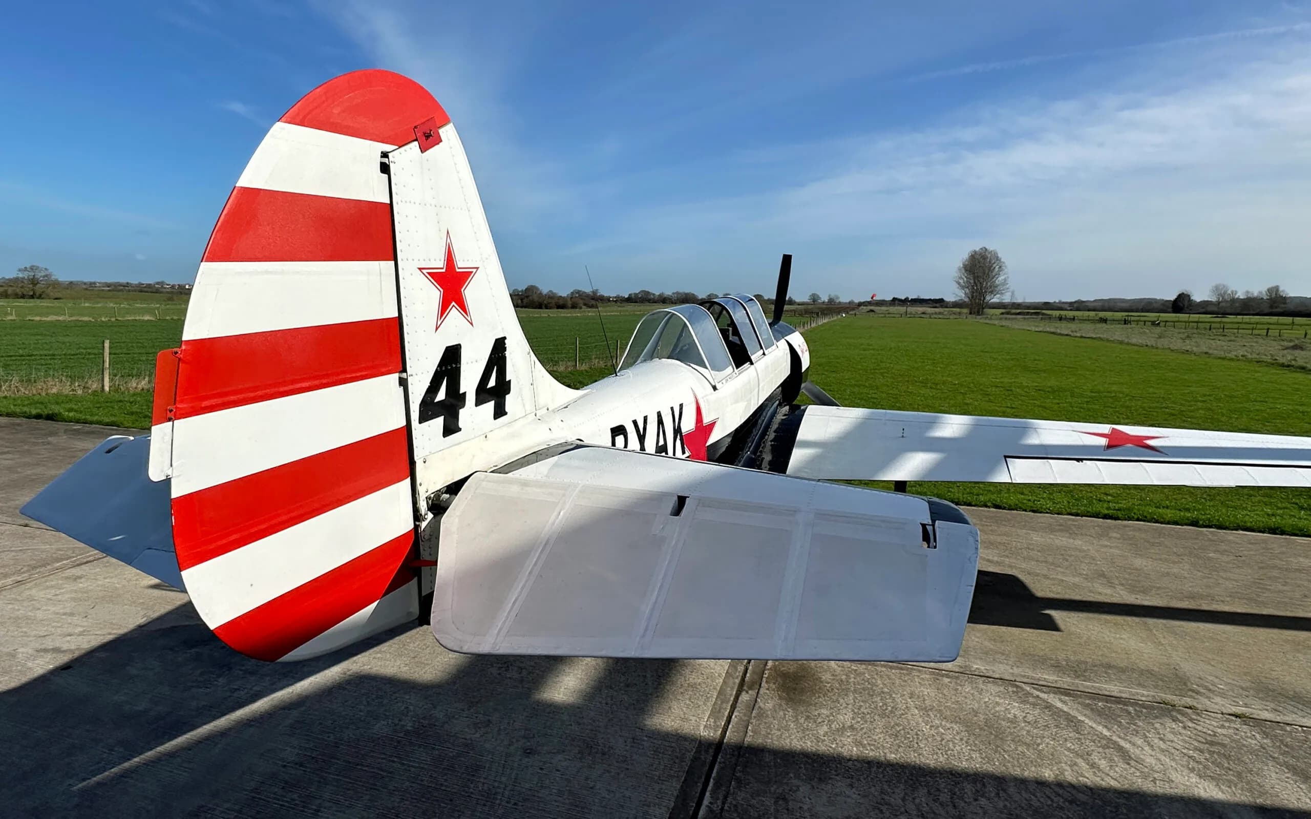 A close-up view of the tail of a Yak-52 aircraft, featuring red and white stripes and the number 44.