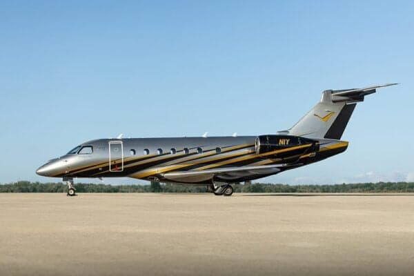 A side view of the N1Y Embraer Legacy 500 private jet with silver, black, and yellow paint on a tarmac.