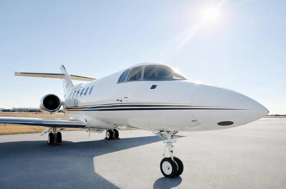 The front section of a white Cessna Citation business jet on an airfield, with the sun shining brightly.