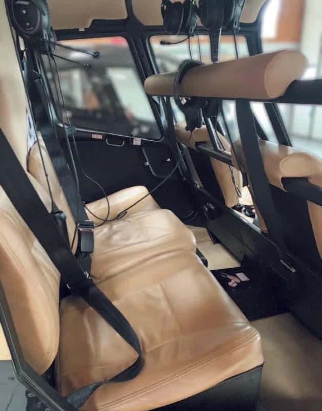 The tan leather seats and seatbelts in the cabin of a helicopter.