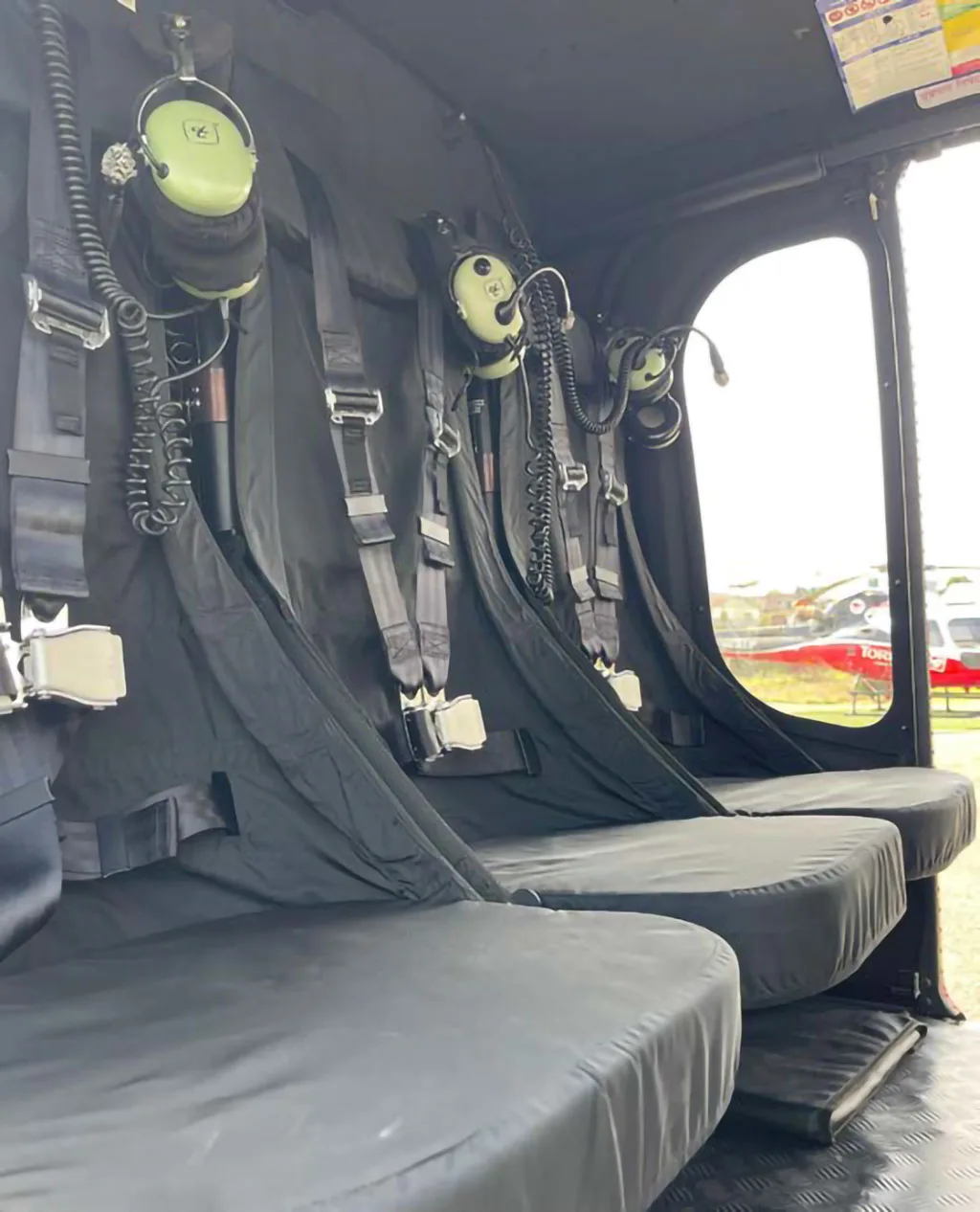 The helicopter's interior shows three black passenger seats with harnesses and communication headsets.