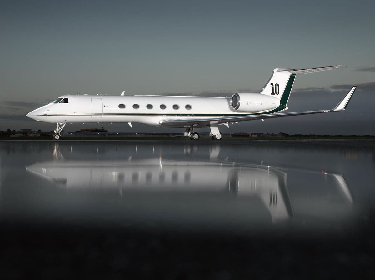 Gulfstream G550 aircraft with tail number 10 parked on a wet tarmac reflecting the sky.