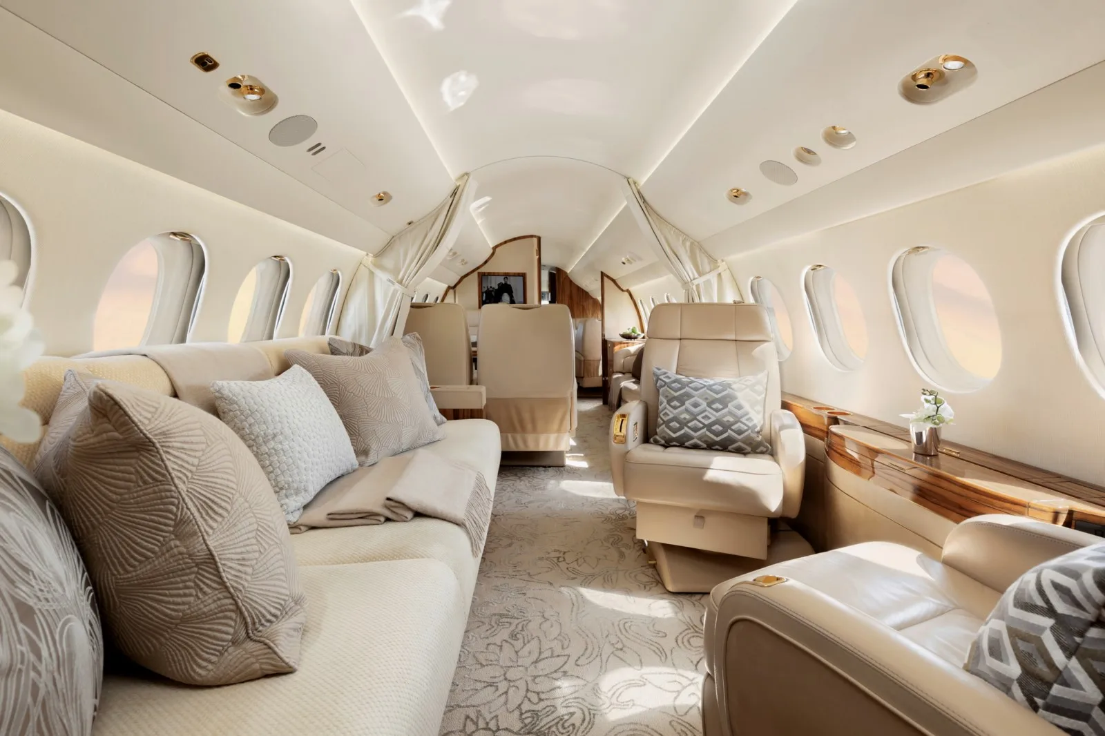 A wide view of the aircraft cabin, showing a cream sofa, individual seats, and a patterned aisle carpet.