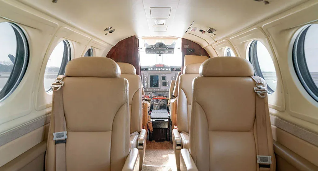 The interior cabin of an aircraft, showing beige leather seats and a view into the cockpit.