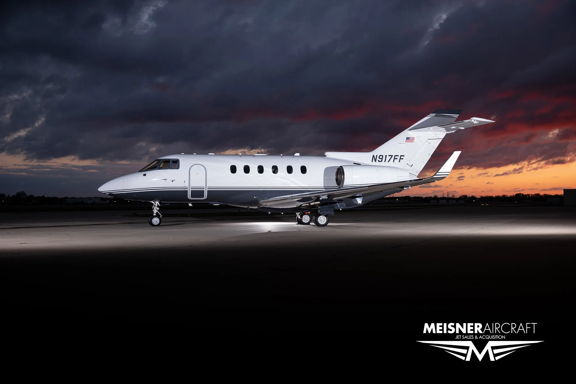 A white and grey business jet (N917FF) parked on a tarmac under a dramatic sky.