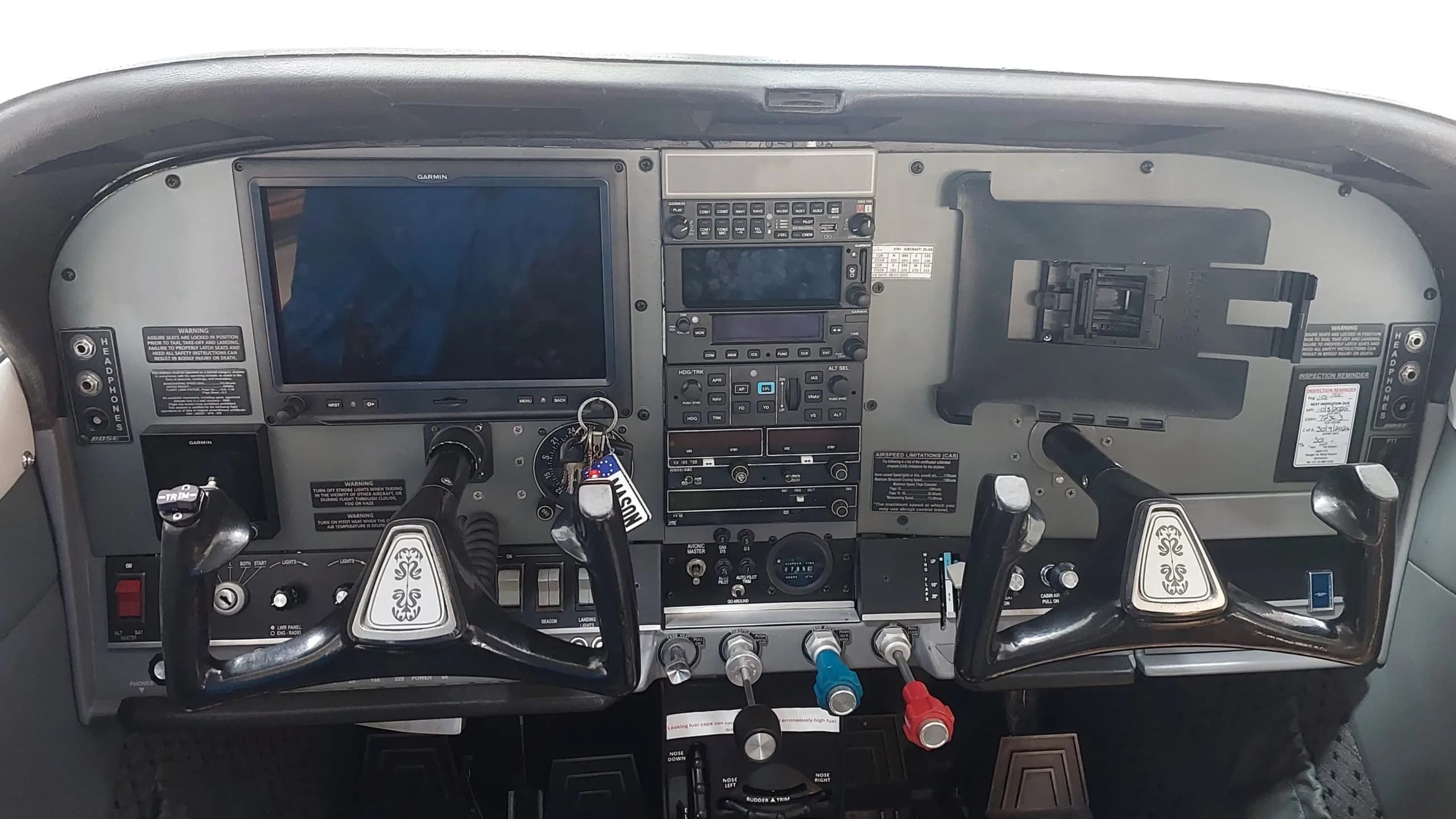 The cockpit of a small aircraft features a modern Garmin display, traditional instruments, and dual yokes.