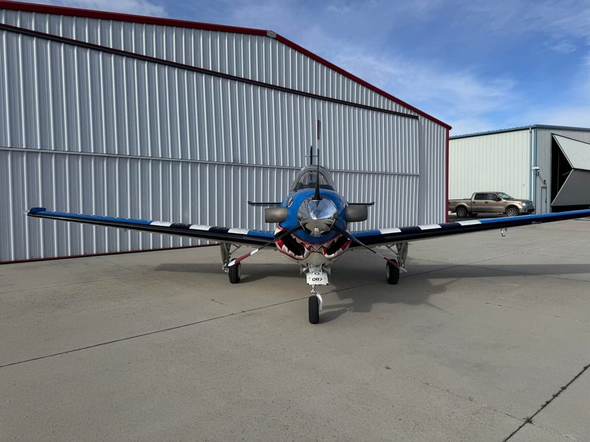 A blue and white SIAI-Marchetti SF.260 is parked on the tarmac with a shark mouth paint scheme.