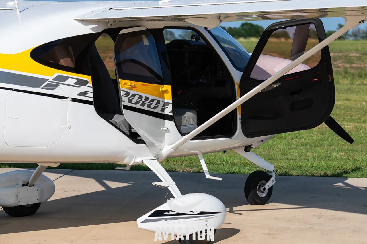 A side view of the front section of a white and yellow Tecnam P2010 TDI aircraft with both cabin doors open.
