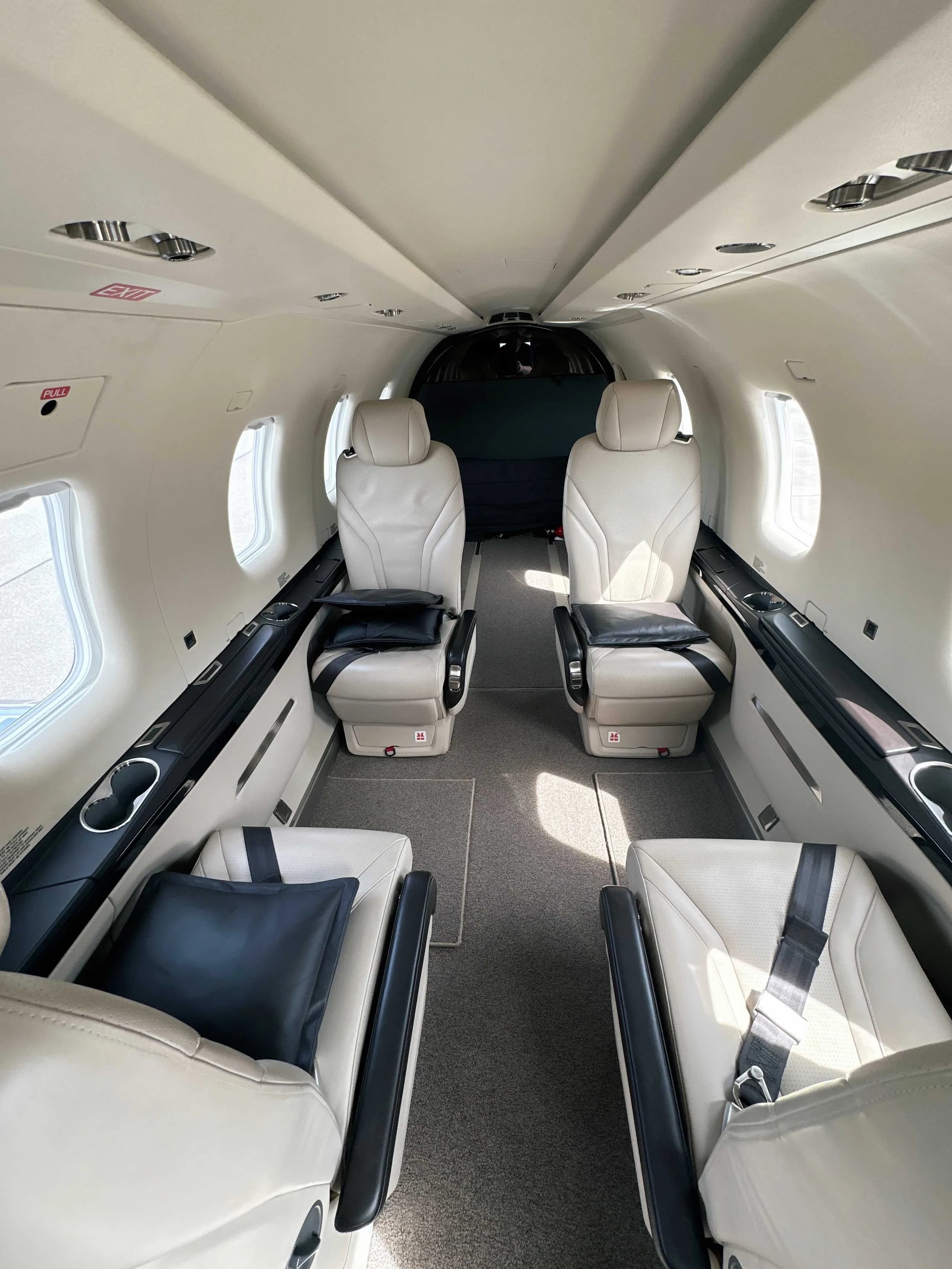 The interior cabin of an aircraft with four light-colored leather seats and dark pillows, facing forward.