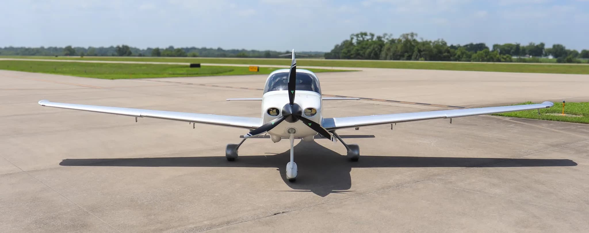 A white Cirrus SR20 X Edition aircraft parked on an airfield with a clear blue sky.