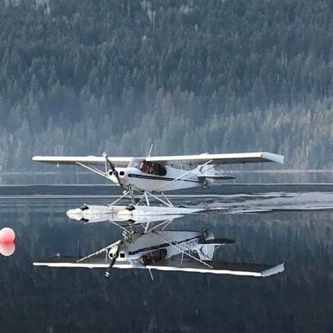 A white and blue Super Cub floatplane on the water with a reflection.