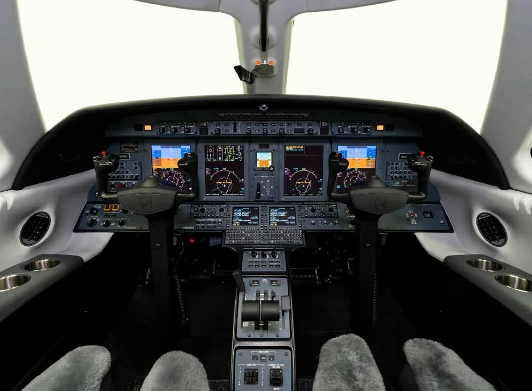 The modern glass cockpit of a business jet, featuring multiple display screens and control yokes.