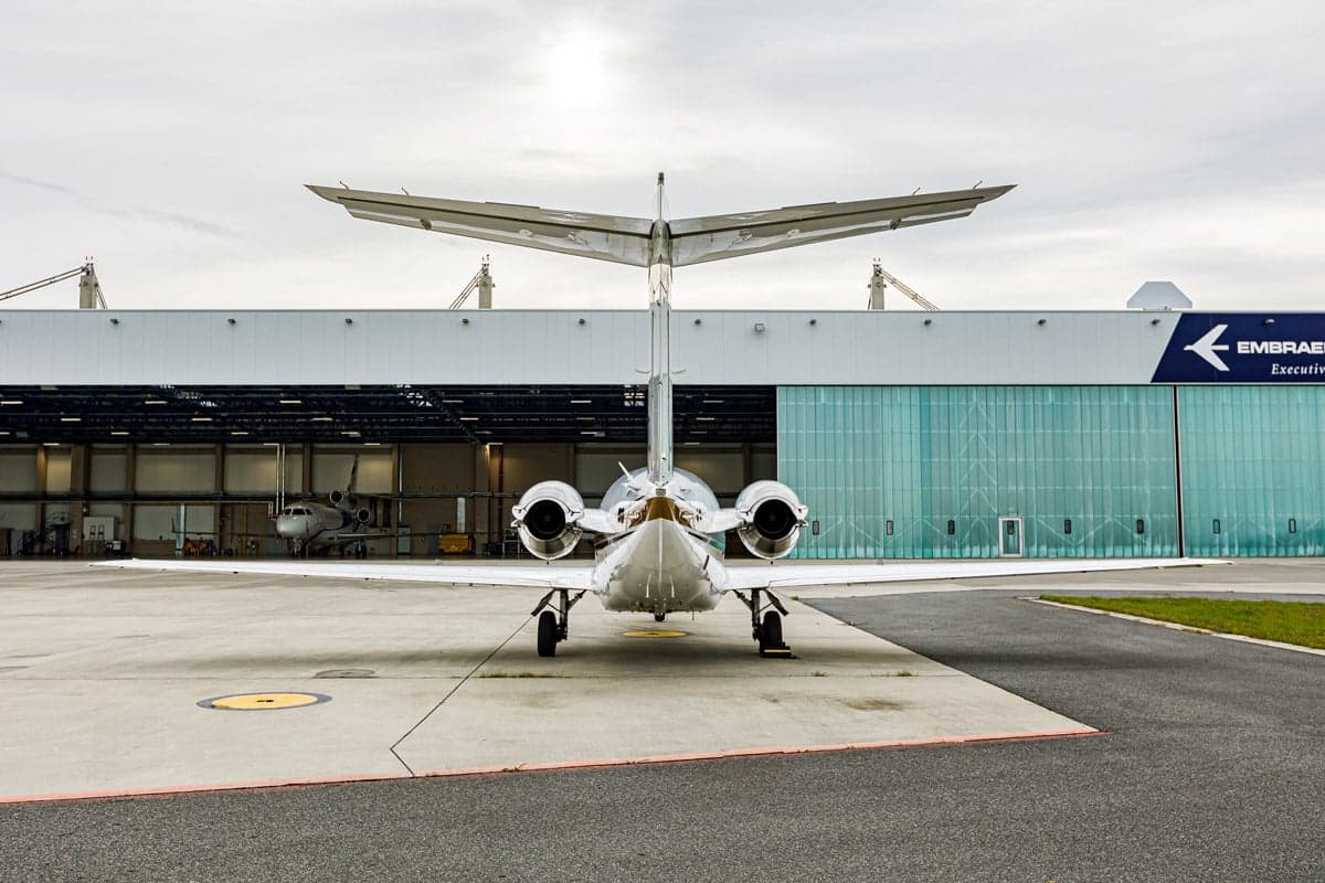 Rear view of the Beechjet 400A aircraft with registration OK-IMO parked in front of an Embraer hangar.