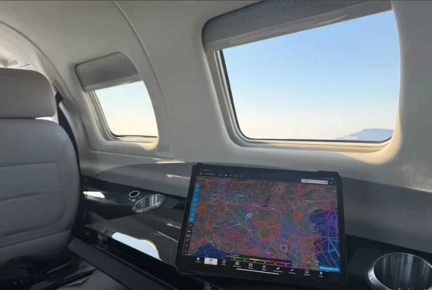 The aircraft's cabin interior with light grey seats, a table, and a tablet displaying an aviation map.