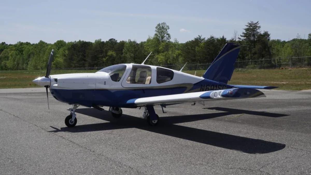 A front-right view of a white and blue single-engine aircraft parked on an airfield.