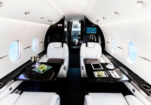 The interior of a Hawker jet with white leather seats and black tables.