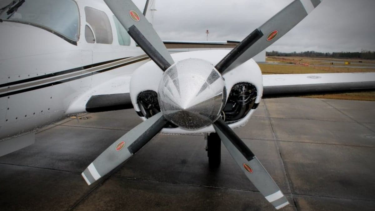 Close-up of the propeller and nose of a white aircraft on a wet tarmac.