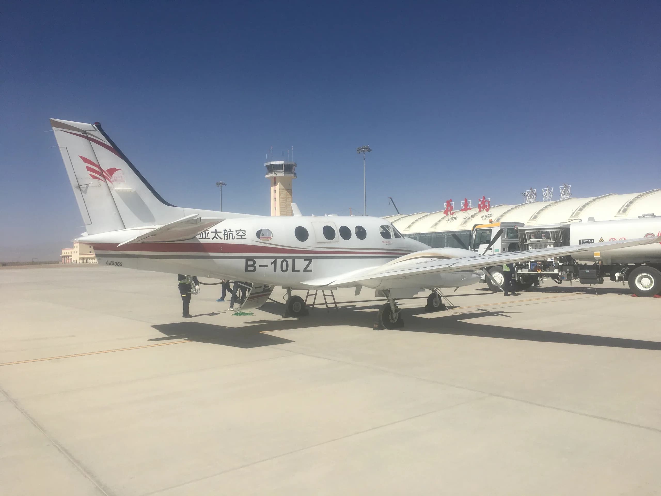 A King Air B-10LZ aircraft is parked on the tarmac next to a fuel truck and airport control tower.