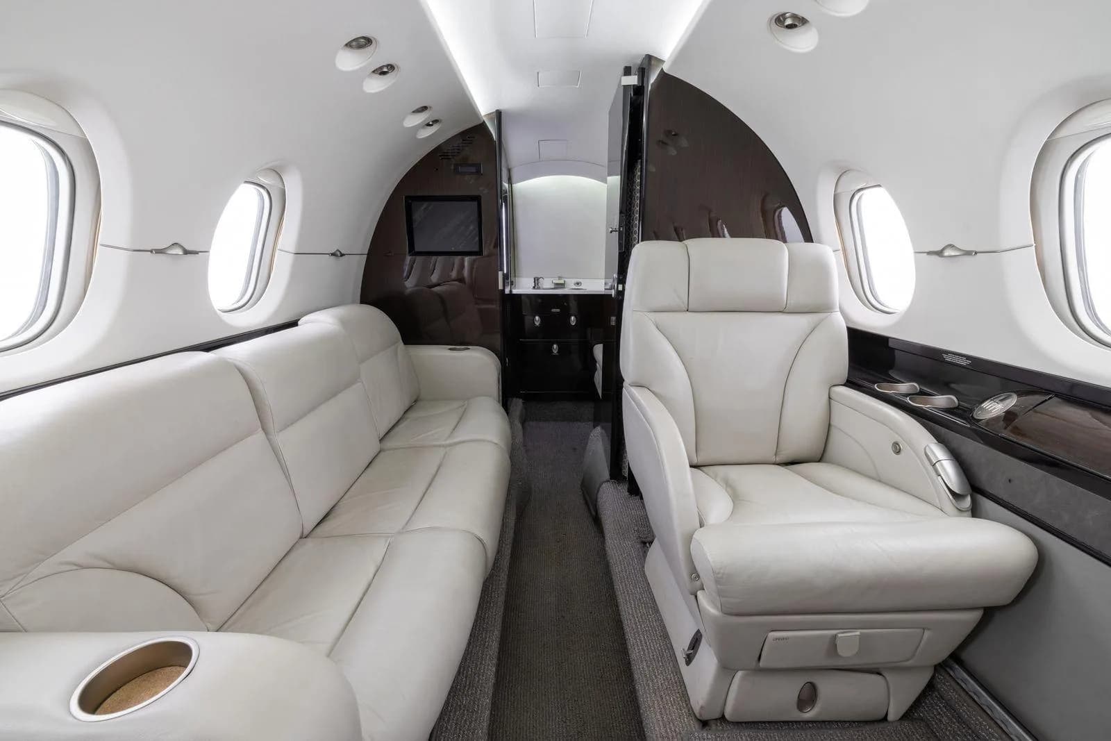 The aircraft's cabin interior with a cream-colored leather sofa and a single executive seat.