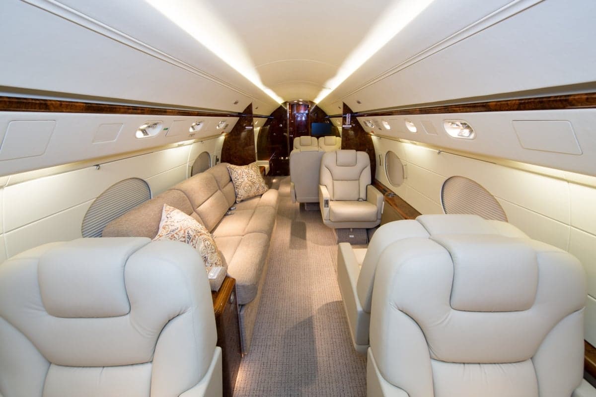 A luxurious aircraft cabin with light-colored leather seats, a beige sofa, and polished wood accents.