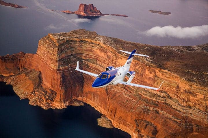 A HondaJet flying over a canyon and lake.