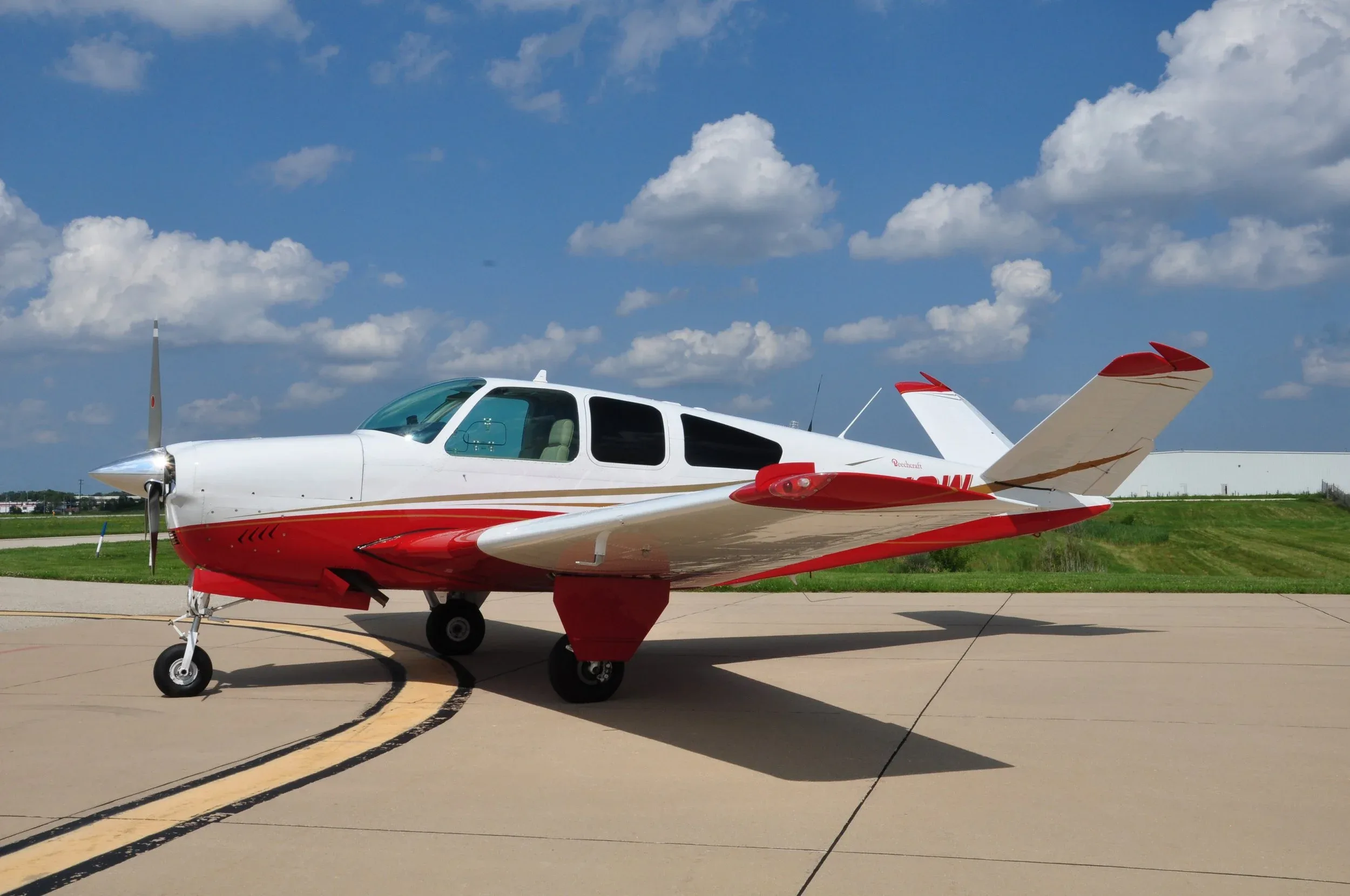 A white and red single-engine propeller aircraft is parked on an asphalt runway under a blue sky with white clouds.