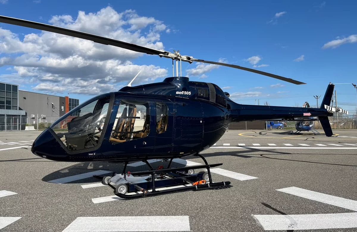 A dark blue Bell 505 helicopter sits on the tarmac.