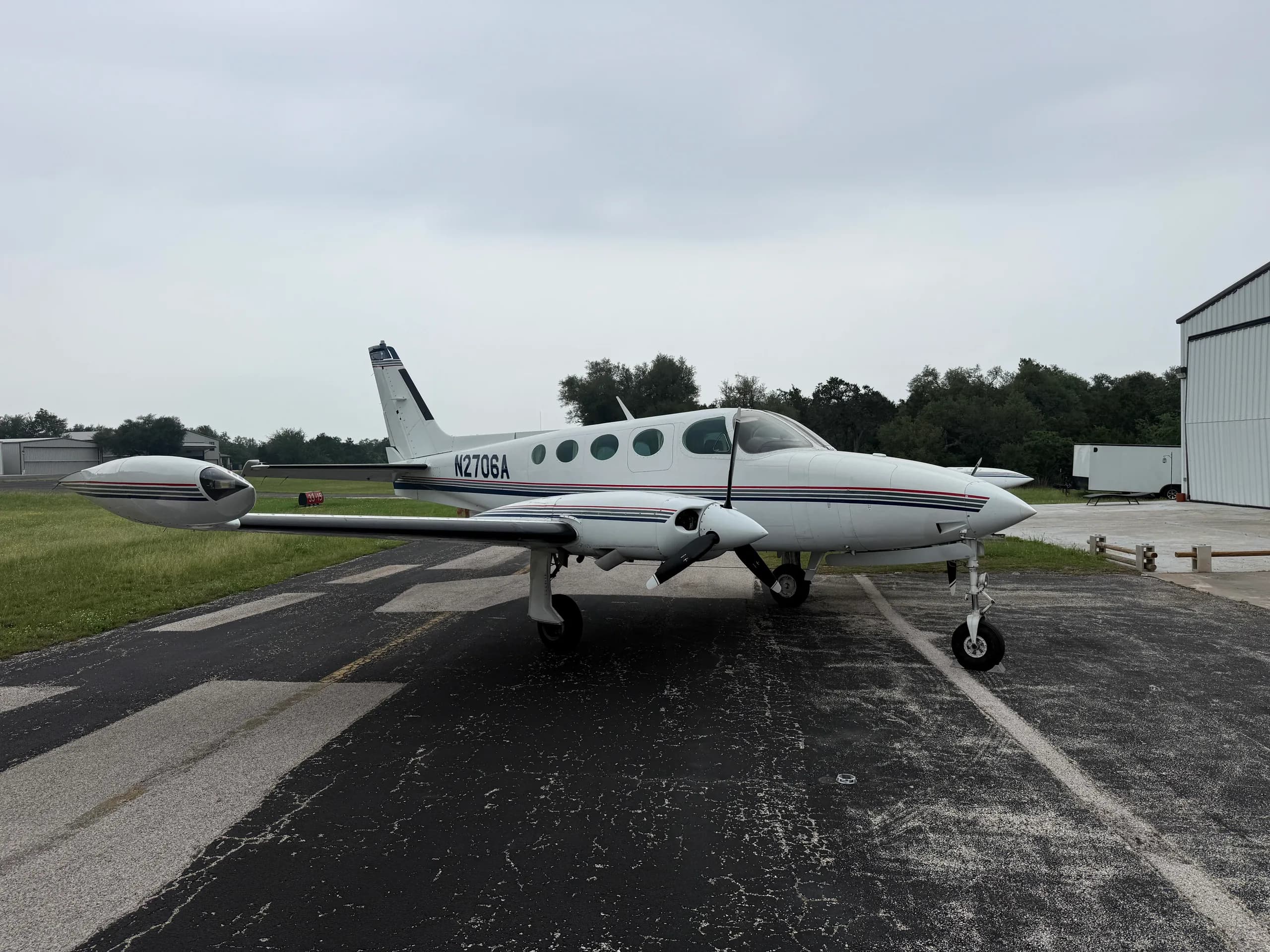 A white Cessna 335 aircraft with blue and red stripes, registration N2706A, parked on an airfield.