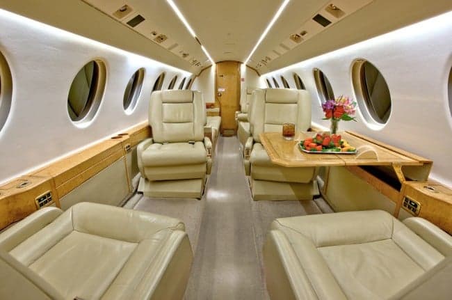 The interior of the aircraft features leather seats, wood trim, and a table with refreshments.