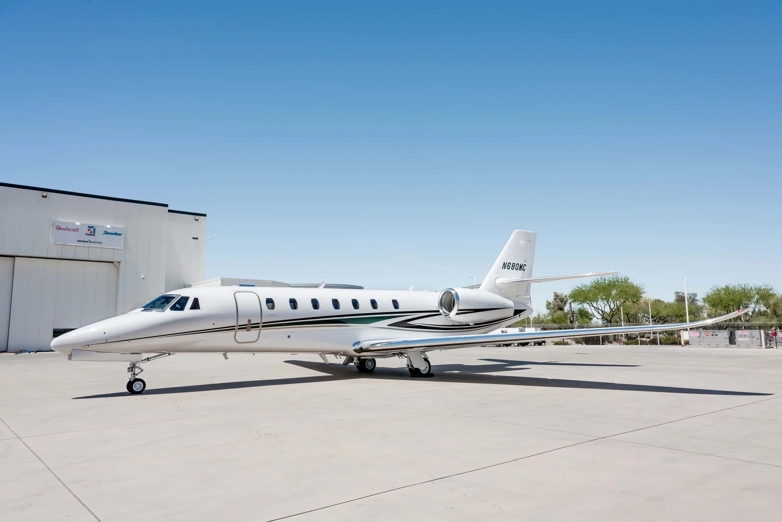 A side view of a white Cessna Citation Latitude business jet, registration N680MC, parked on a tarmac next to a hangar.