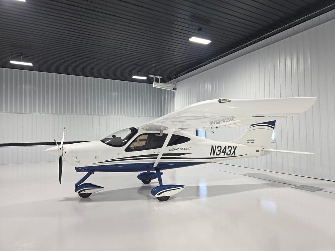 A white and blue Tecnam P2008 Light Sport aircraft (N343X) is parked inside a clean hangar.