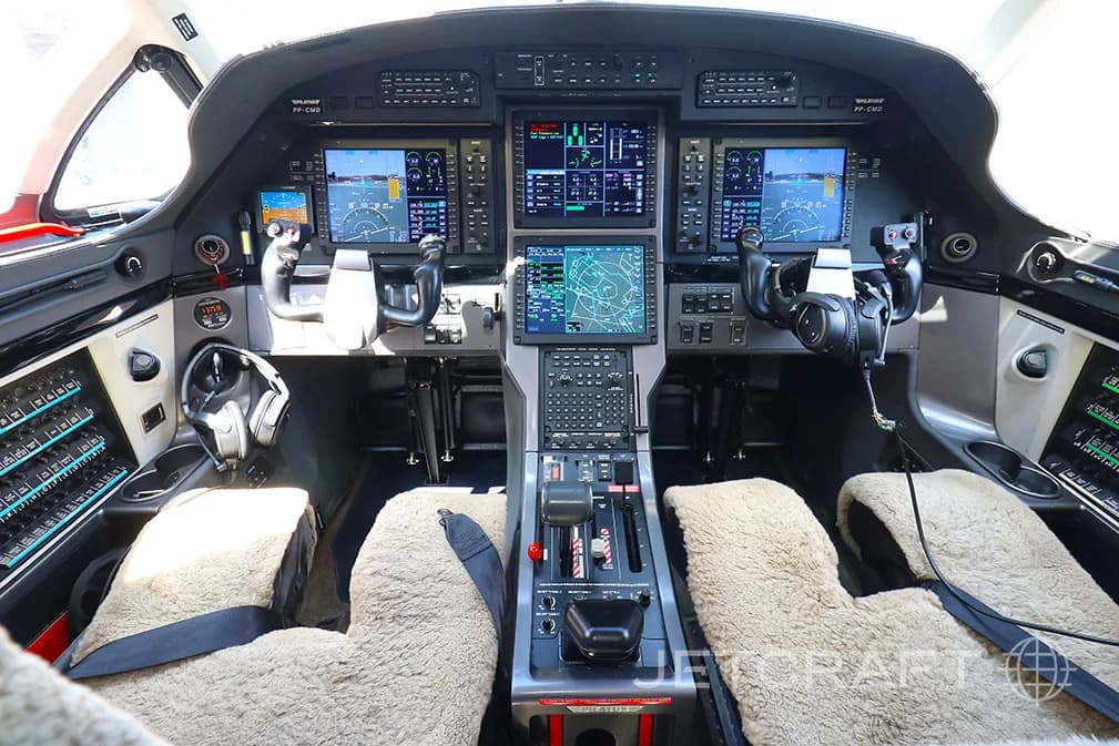 The modern cockpit of a Pilatus PC-12 NGX aircraft with multiple large digital displays and sheepskin seat covers.