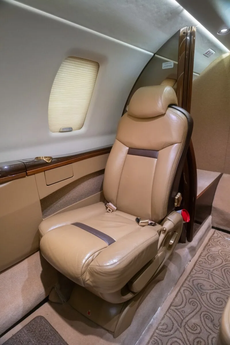 A small tan bench seat and a dark wood cabinet in the aircraft cabin.