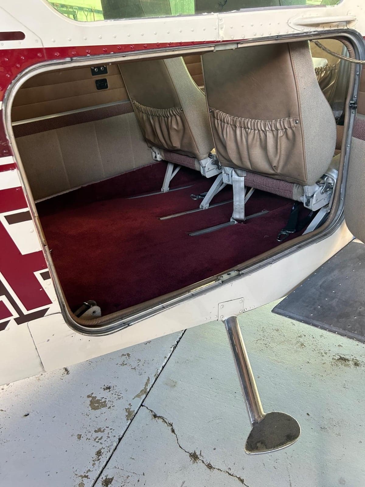 The open rear door of an aircraft showing the red carpeted cabin floor and two rear seats.
