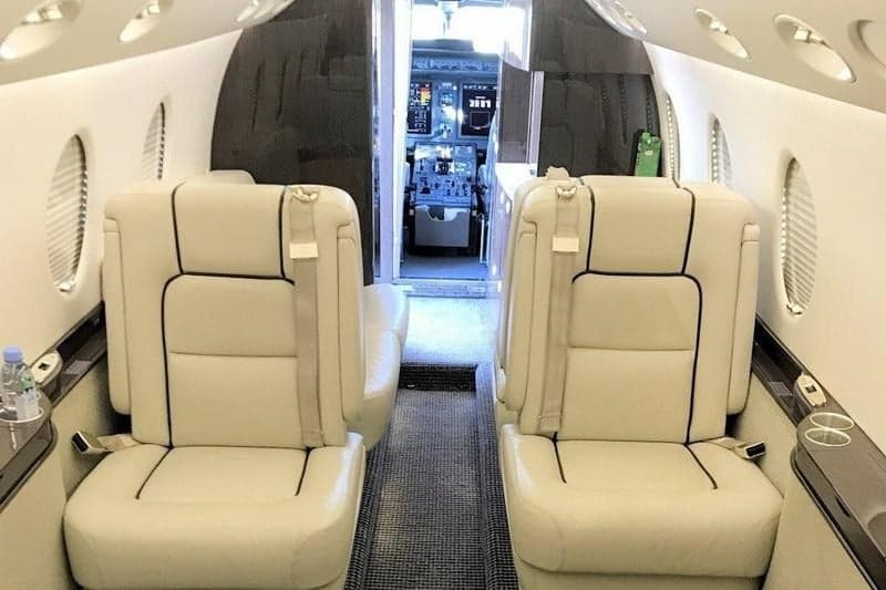 View of the aircraft interior with cream-colored leather seats and a glimpse into the cockpit.