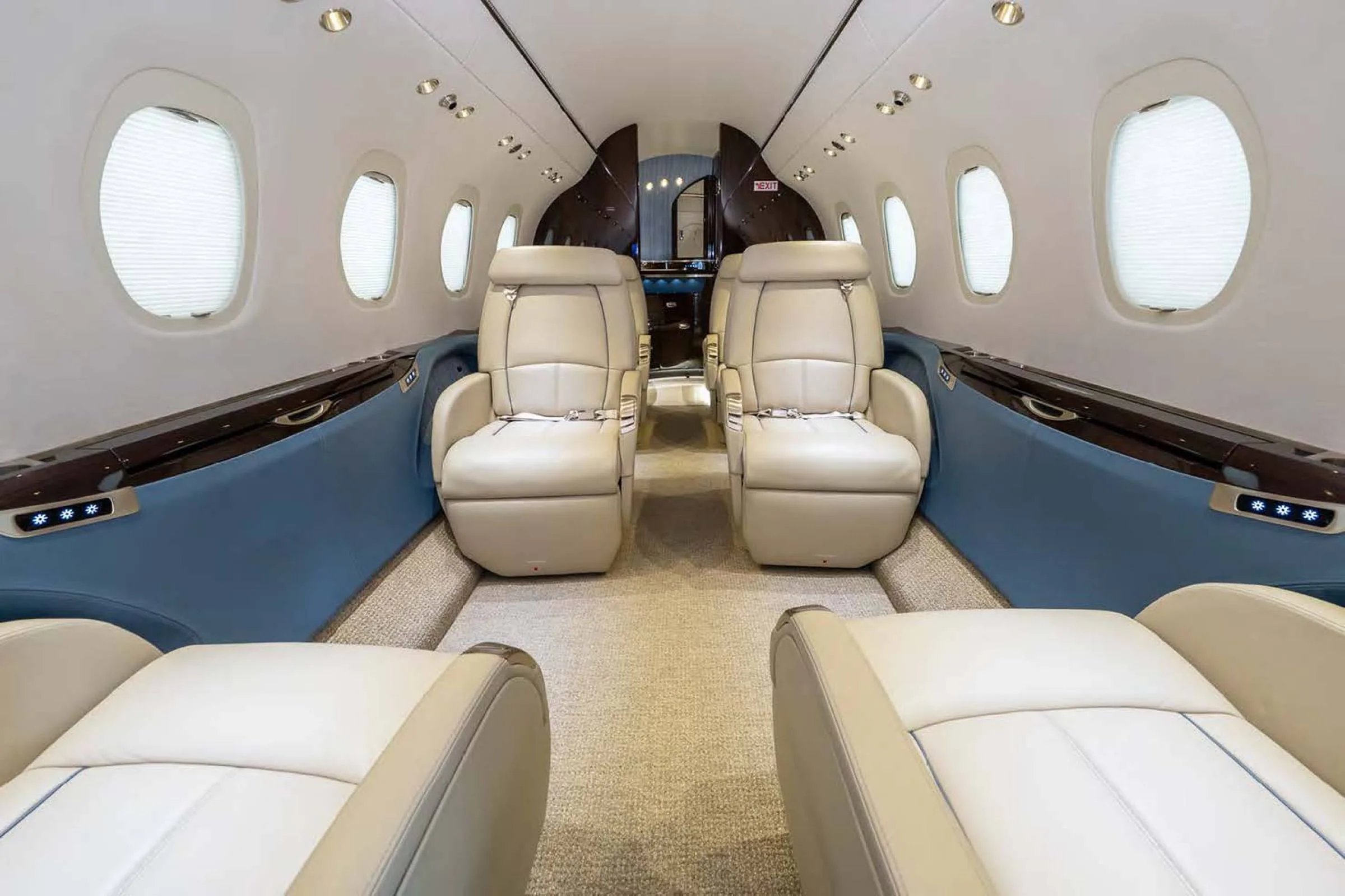 The luxurious interior cabin of a private jet with beige leather seats and blue accents, looking towards the rear.