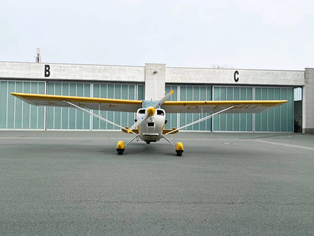 A yellow and white aircraft, D-EIMU, parked on the tarmac next to a building.