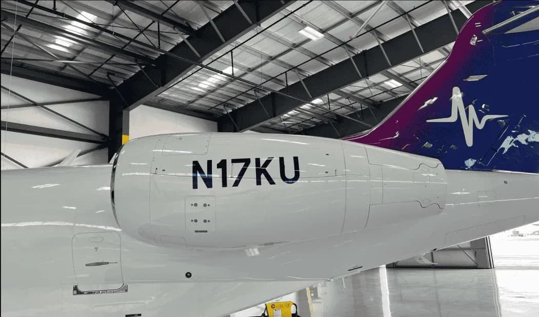 A close-up of the engine and tail section of a white business jet, showing the registration N17KU and a purple and blue heartbeat tail livery, inside a hangar.
