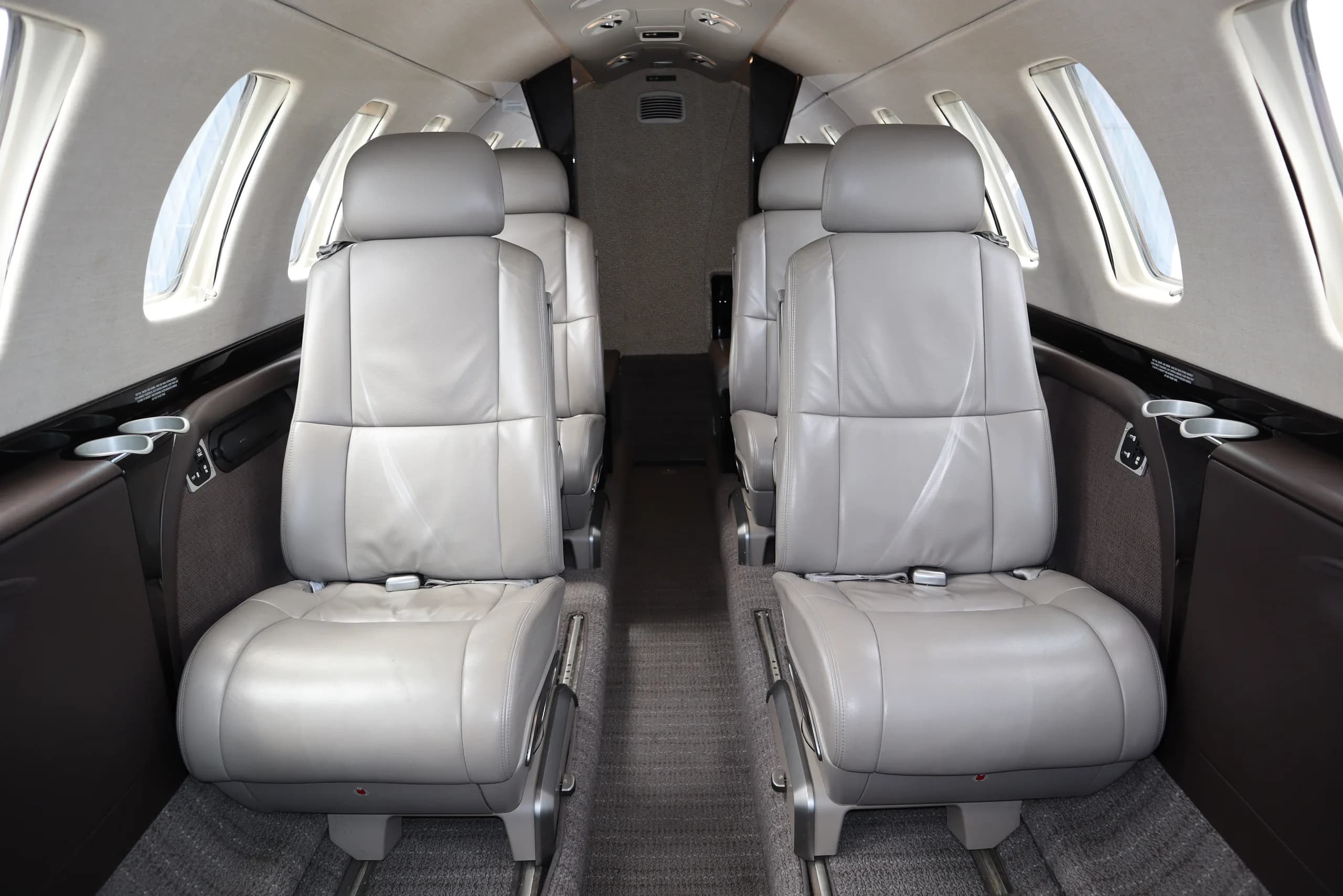 A close-up view of two rows of grey leather seats in the cabin of a business jet, facing forward.