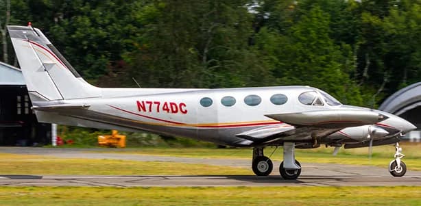 A silver and white Beechcraft King Air with red accents taxis on the runway.