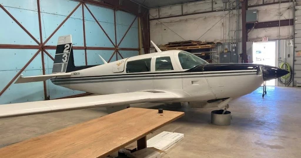 Side view of a white and black Grumman American AA-5 Traveler aircraft, N1047A, inside a hangar.