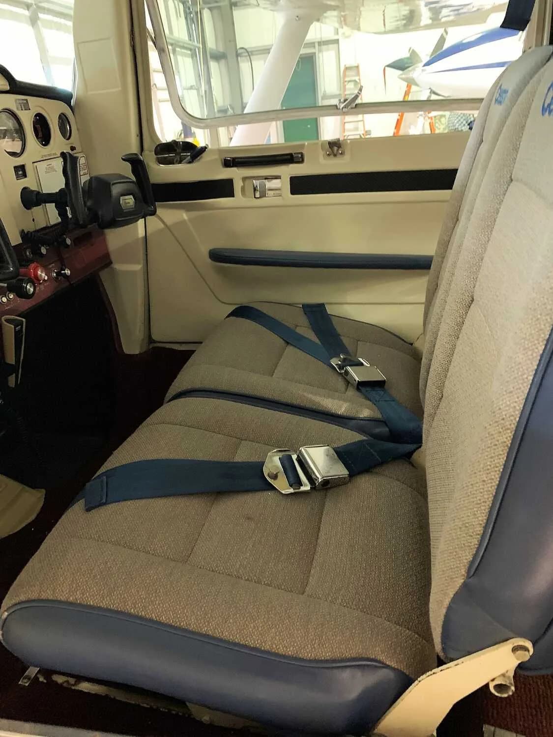 Front seats of a Cessna 172 Skyhawk with blue seatbelts.