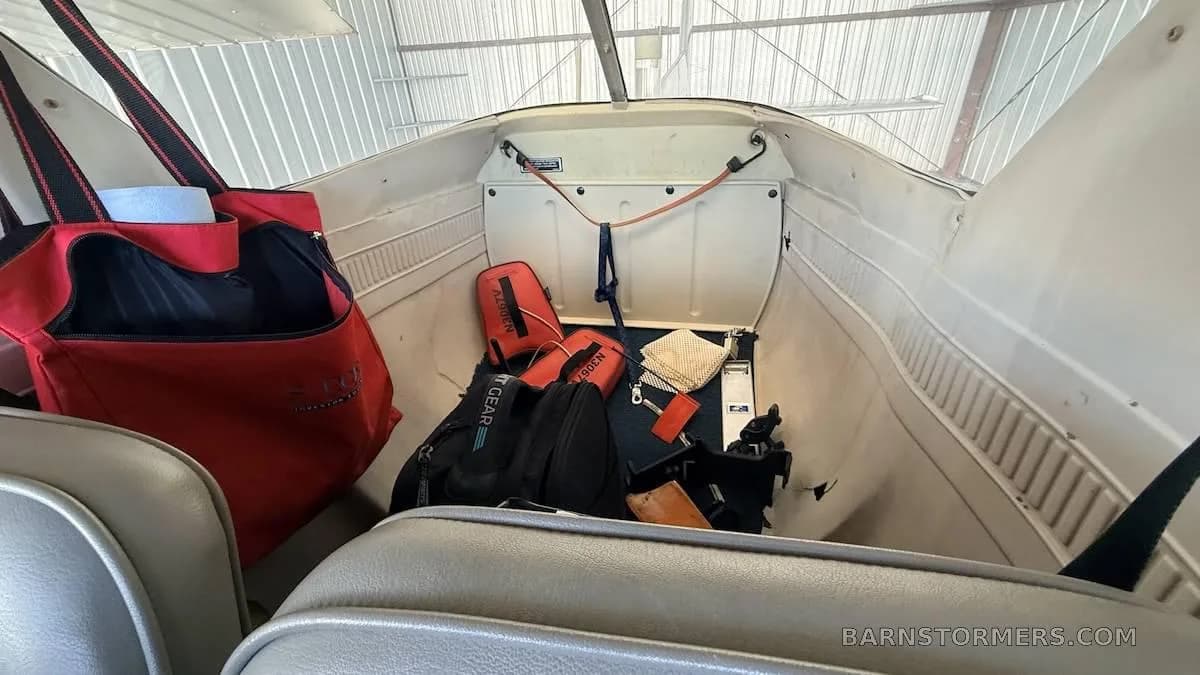 The aircraft's baggage compartment behind the seats, containing various items and a red bag.