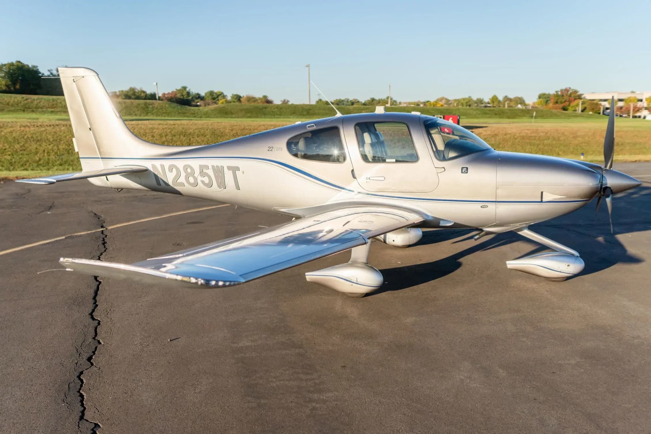 A side view of the silver and grey Cirrus SR22 aircraft (N285WT) with blue accent stripes on an asphalt tarmac.
