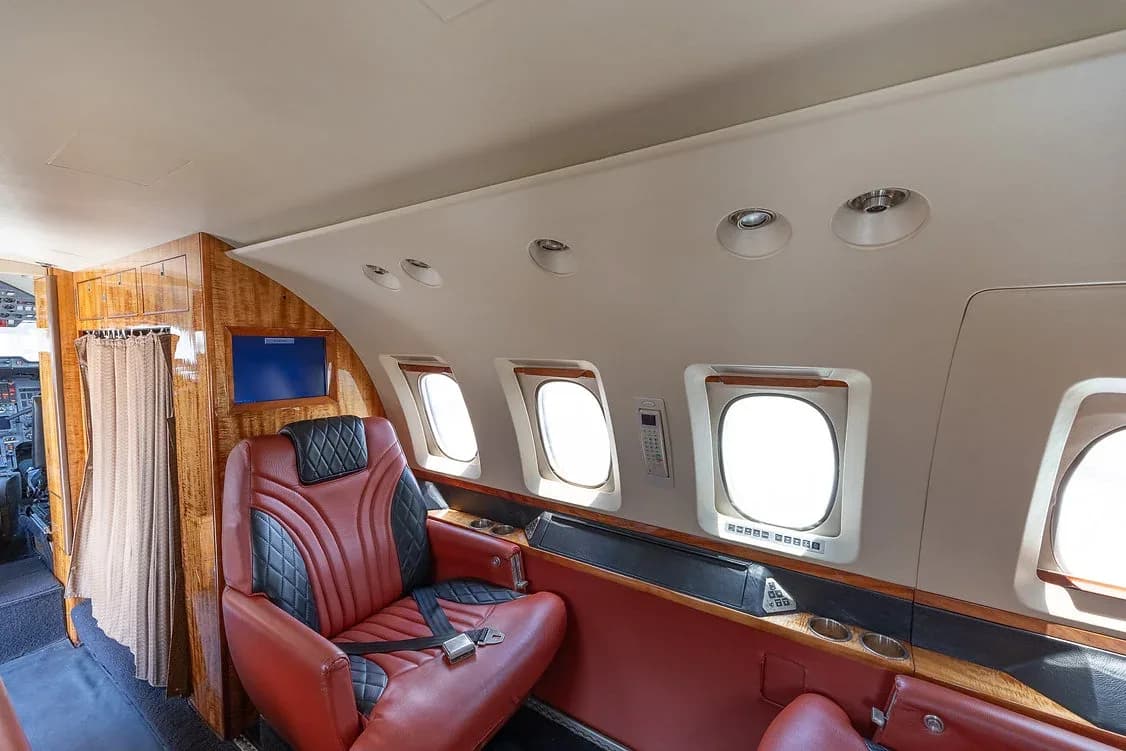 A single red and black leather seat in the private jet's cabin, with windows and wood paneling along the side.