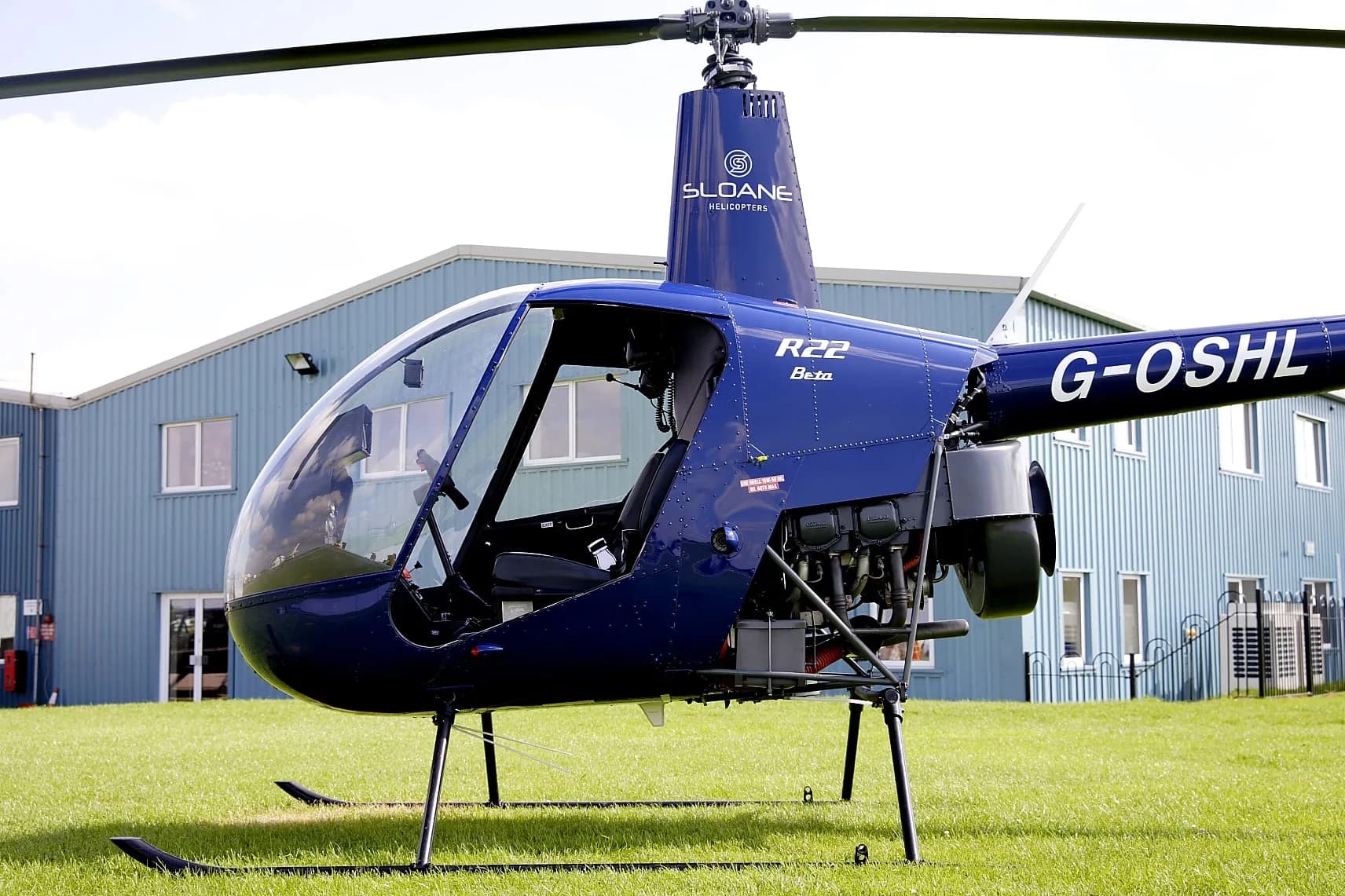 Side view of a blue Robinson R22 helicopter on the ground in front of a building.